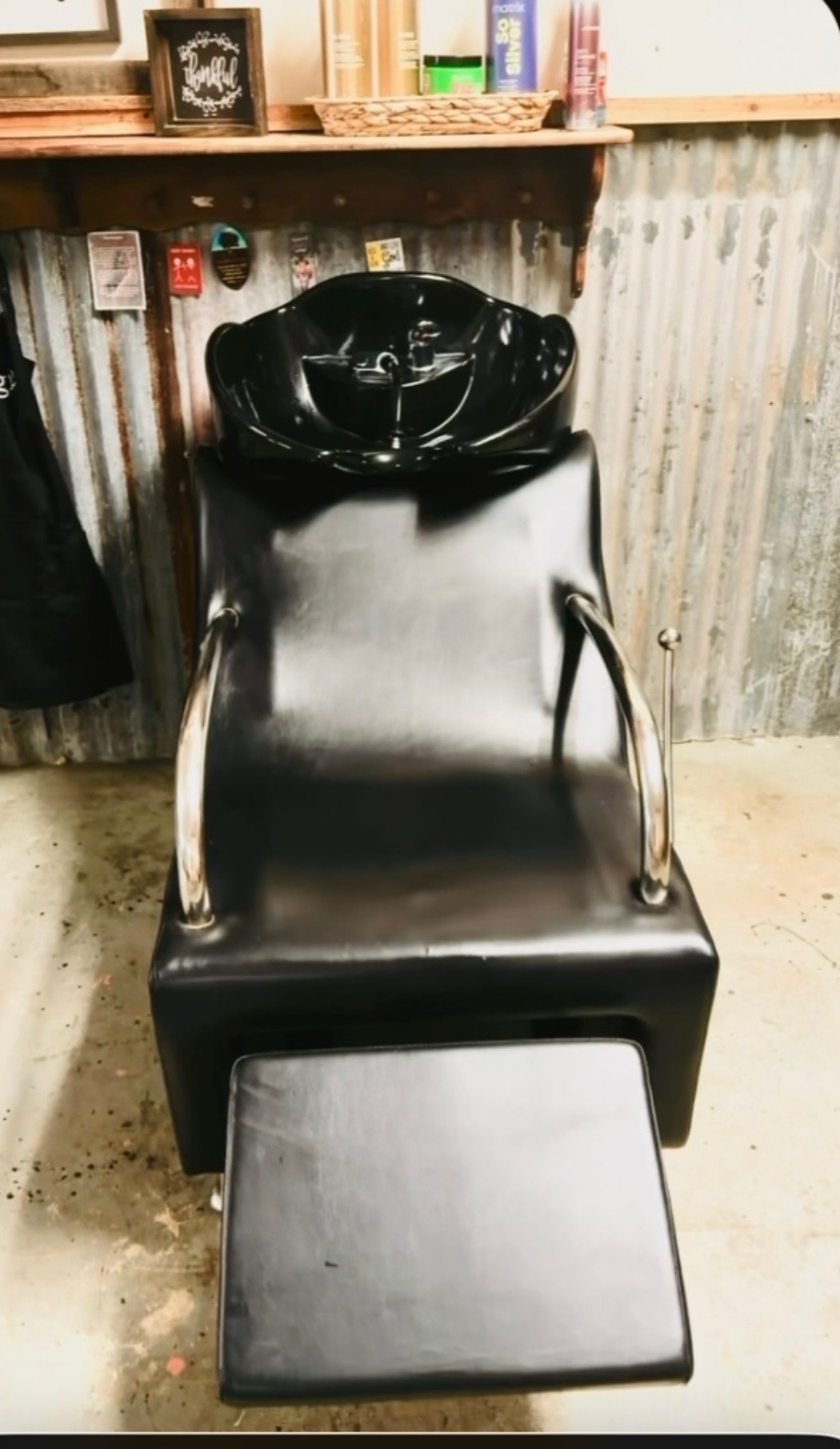 Shampoo station with a black wash bowl and reclining chair against the corrugated-metal wall