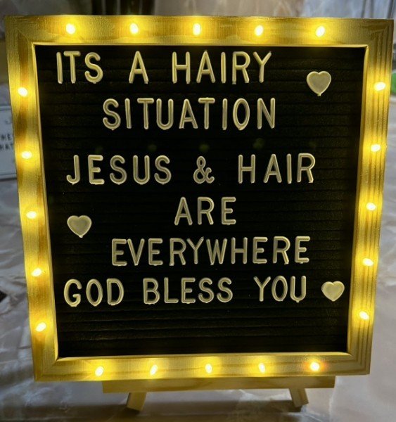 Lighted letter board in the salon reading It’s a hairy situation — Jesus and hair are everywhere — God bless you